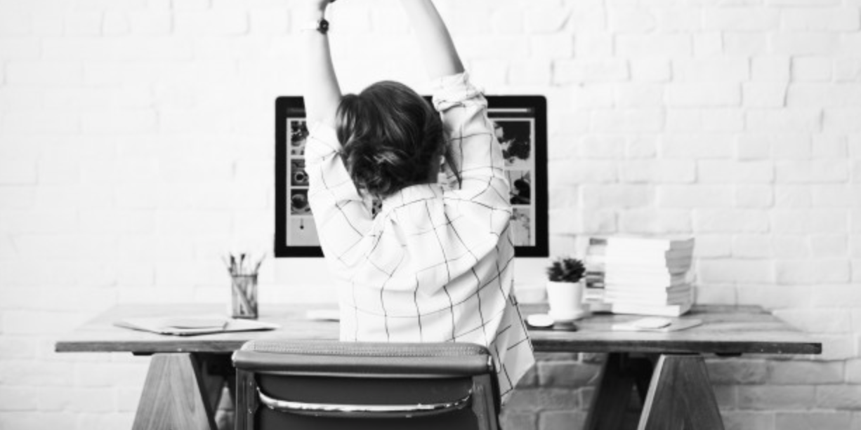 Woman stretching at her desk with her arms up in the air